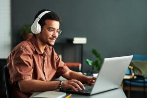 Jovem estudando em casa com fones de ouvido e laptop, demonstrando concentração e dedicação. A imagem representa uma pessoa explorando métodos autodidatas, como aprender inglês sozinho através de aulas online.