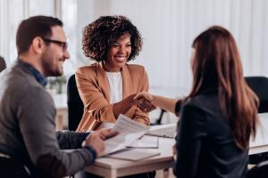 Candidata jovem em entrevista de emprego sorrindo e cumprimentando recrutadora após apresentar currículo sem experiência. 