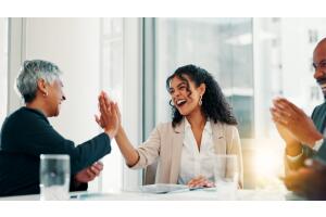 Mulher jovem sorridente recebe um high five de colega em ambiente corporativo, sendo reconhecida por seu desempenho. A imagem representa inteligência emocional no trabalho e o impacto positivo nas relações profissionais