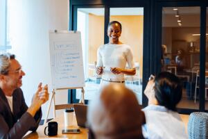 Jovem profissional apresenta quadro com soft skills como comunicação e trabalho em equipe durante treinamento corporativo, ilustrando a importância das habilidades comportamentais no início da carreira.