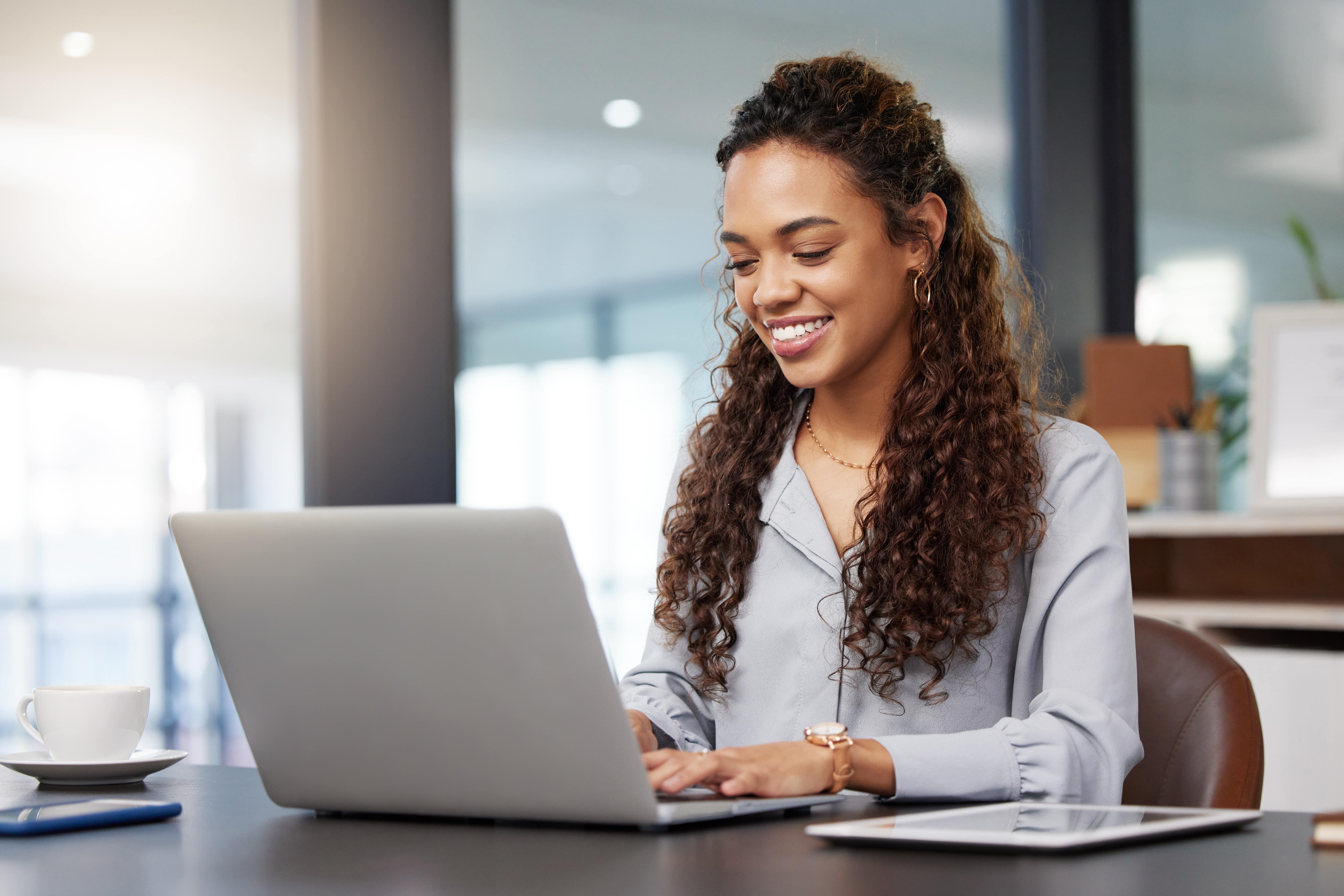 Jovem sorridente usando notebook em ambiente corporativo, representando uma profissional capacitada com domínio do Pacote Office e Excel, habilidades essenciais para o mercado de trabalho.