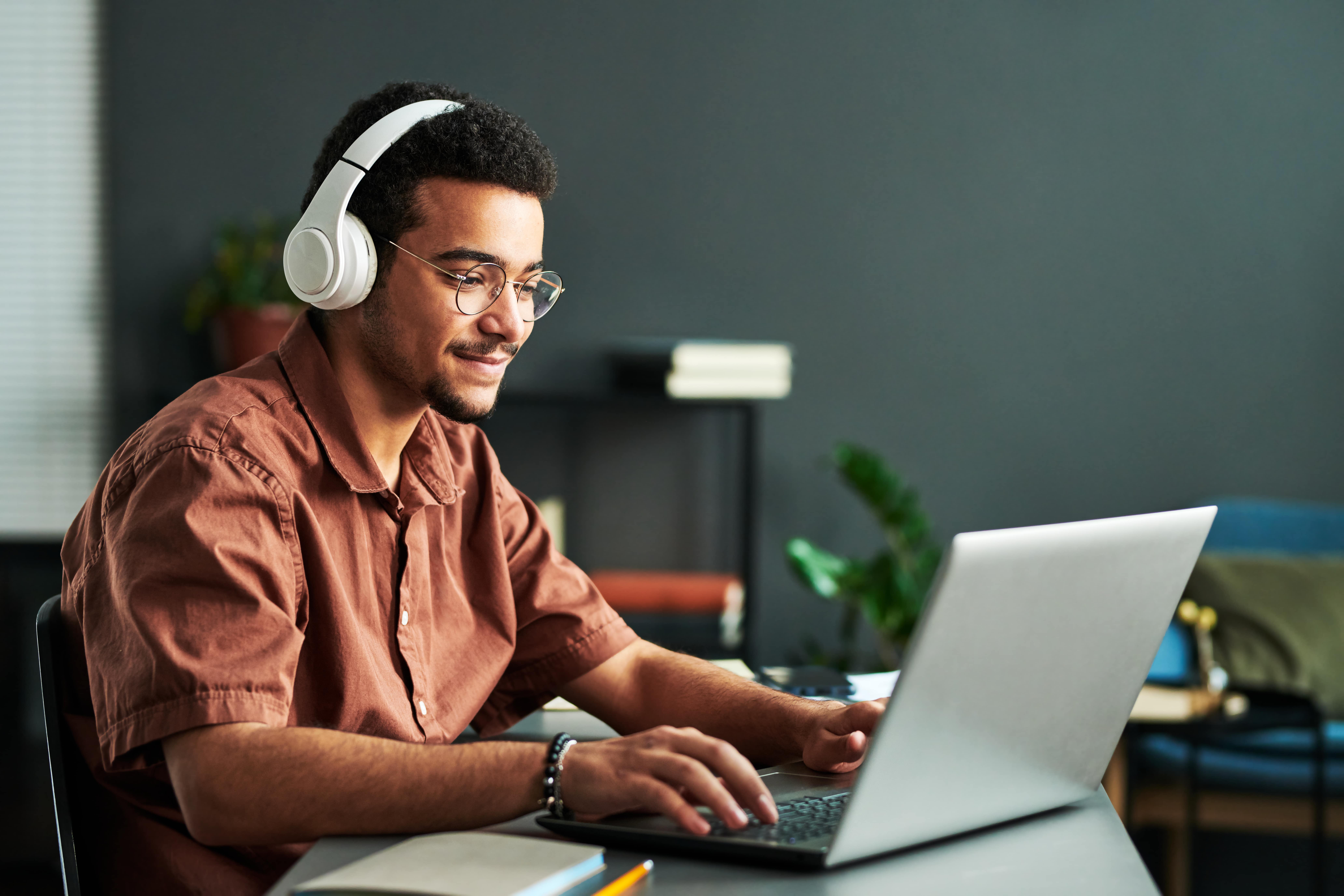 Jovem estudando em casa com fones de ouvido e laptop, demonstrando concentração e dedicação. A imagem representa uma pessoa explorando métodos autodidatas, como aprender inglês sozinho através de aulas online.