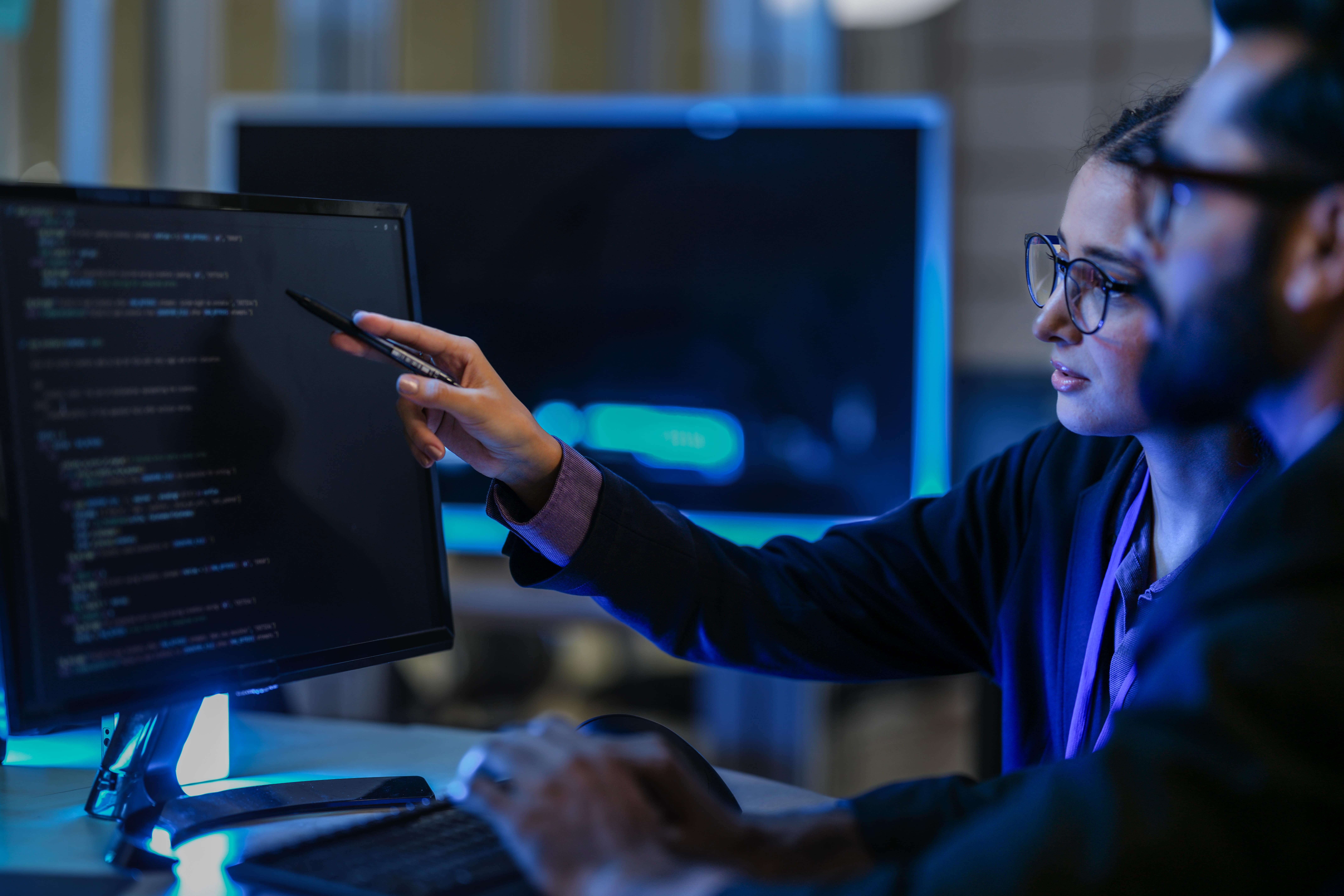 Dupla de profissionais analisando códigos em tela, representando as profissões do futuro nas áreas de programação, análise de dados e tecnologia